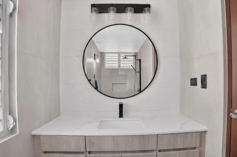 Tocador blanco con espejo circular en un baño renovado en Puerto Rico