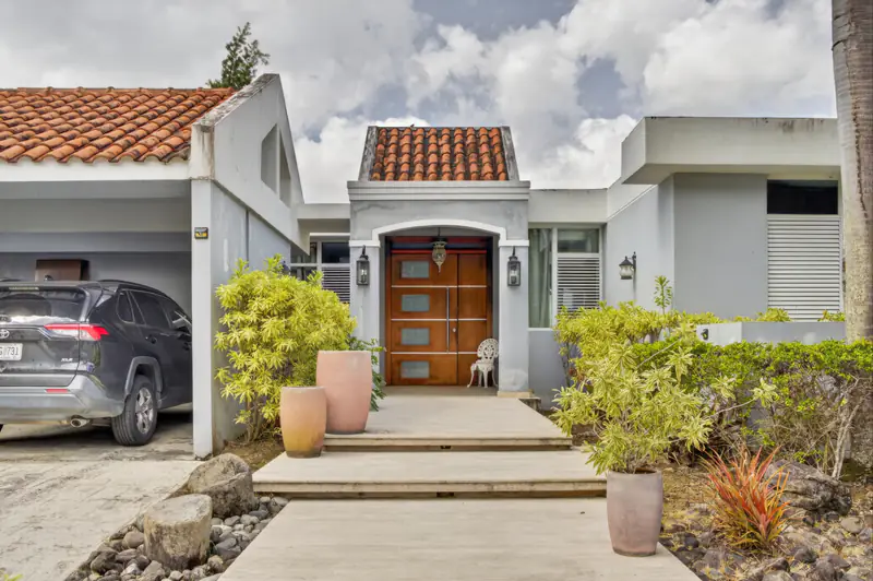 Fachada blanca de una residencia con jardín y entrada escalonada en Puerto Rico